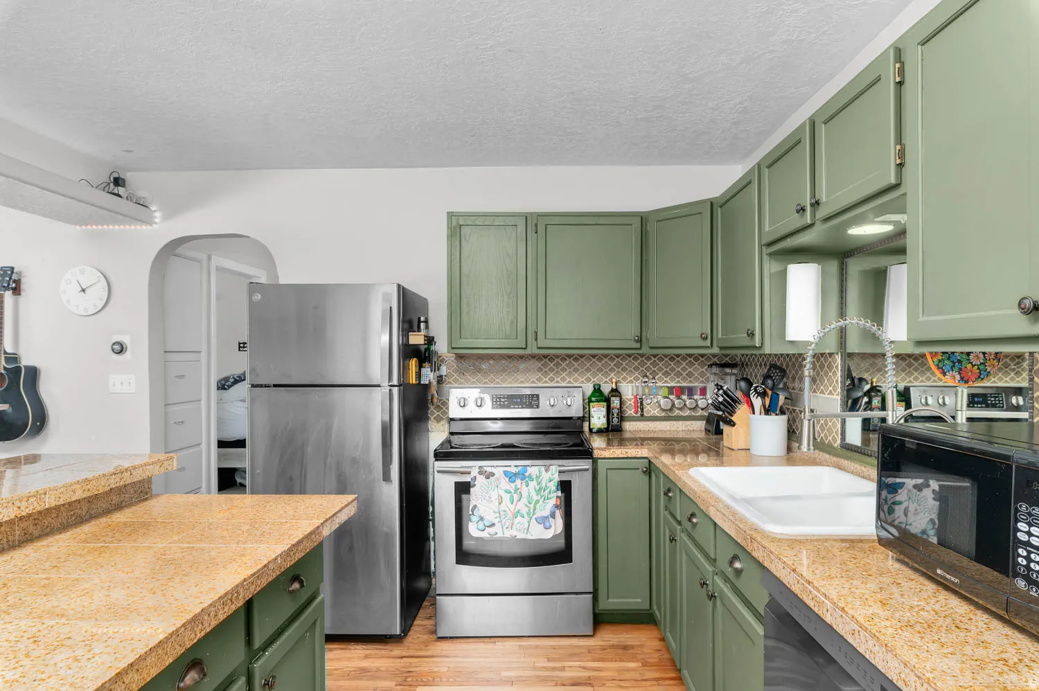 Kitchen featuring green painted cabinetry, granite-style countertops, stainless steel appliances, and a patterned tile backsplash