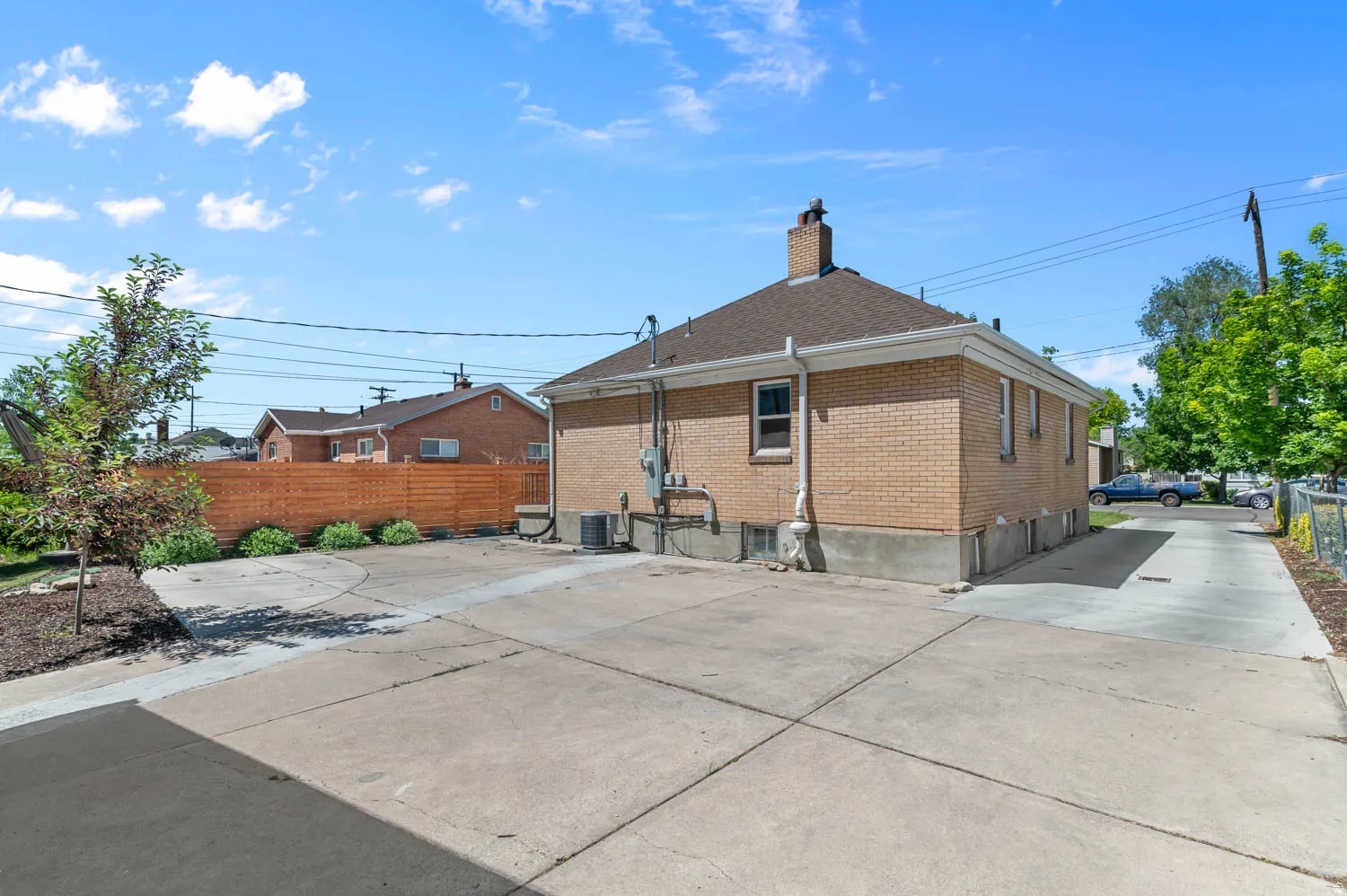 Expansive concrete patio with a brick exterior, shingle roof, and a wood privacy fence