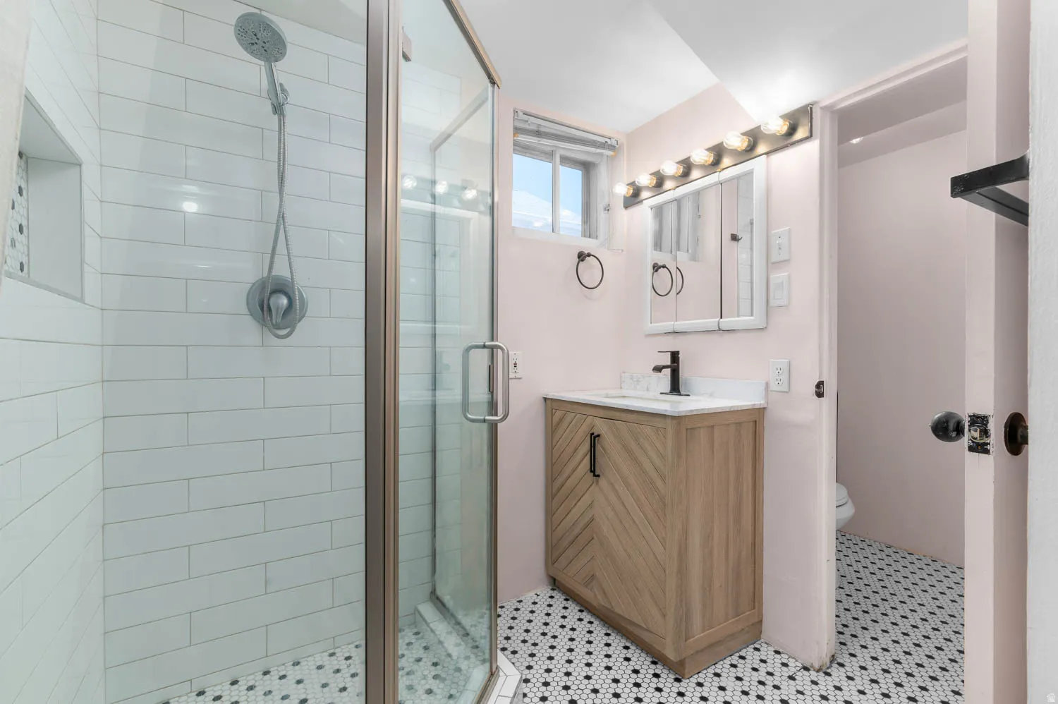 Bathroom featuring a glass-enclosed shower with subway tile, a shower niche, and a black-and-white hexagonal tile floor