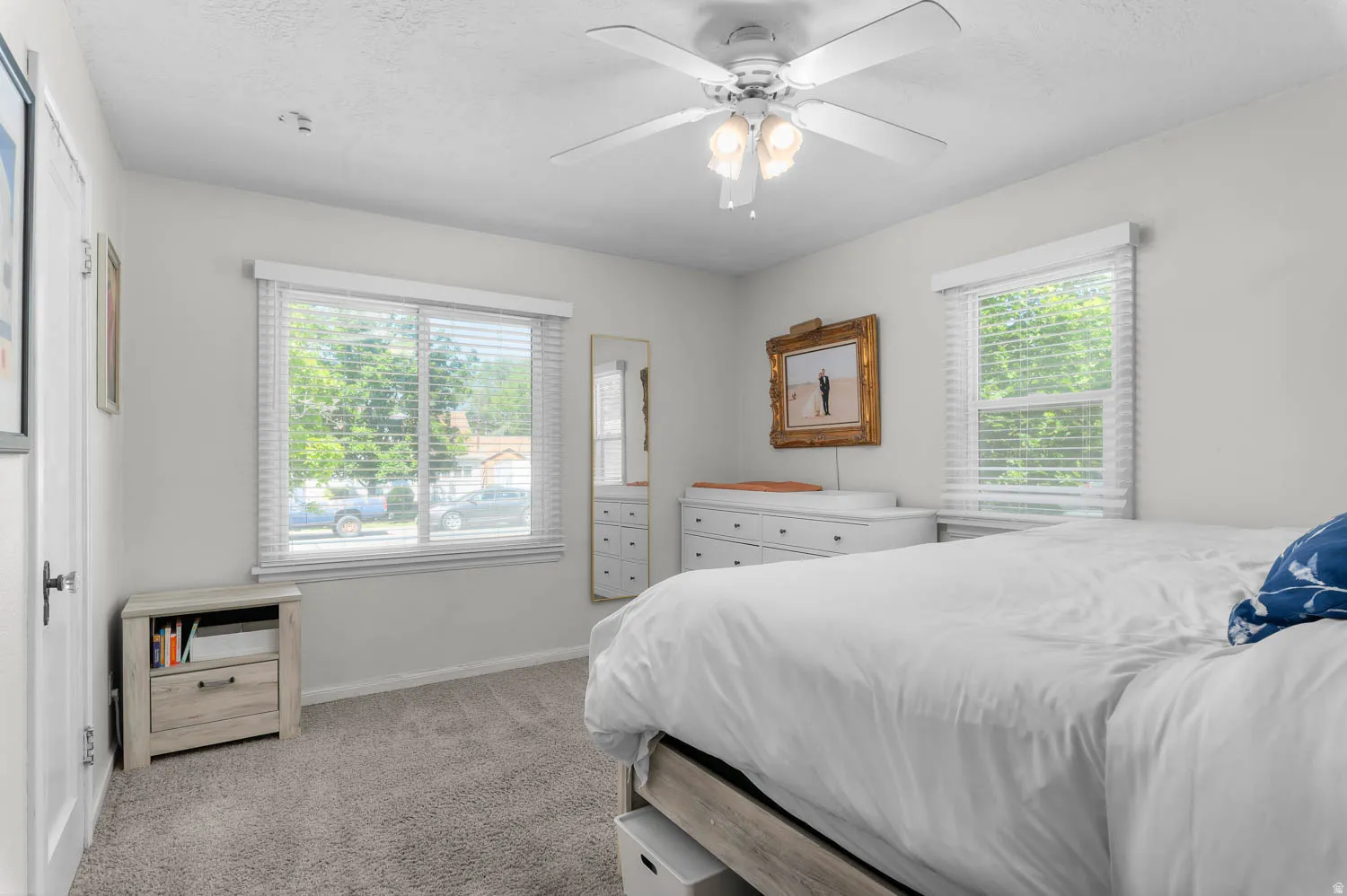 Wall-to-wall carpeting and white walls enhance this space, featuring two windows with horizontal blinds