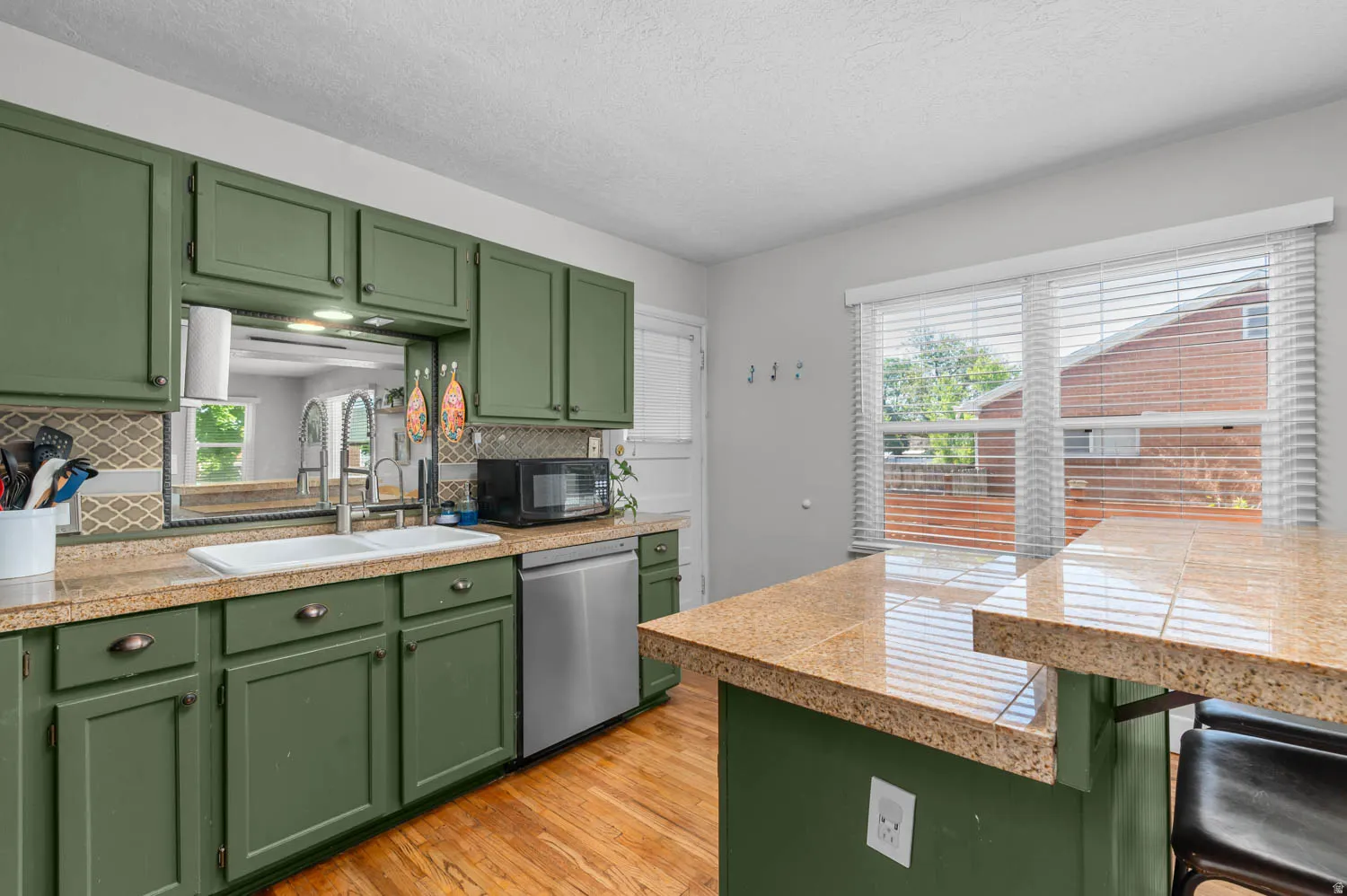 Kitchen featuring green cabinetry, tile countertops, stainless steel dishwasher, tile backsplash, and wood-finish flooring