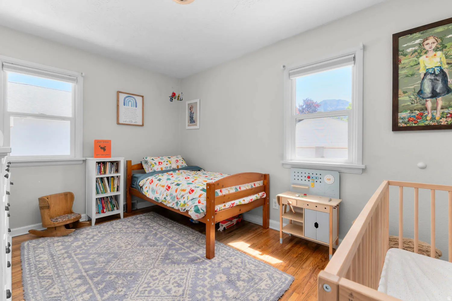 Bright room featuring two windows, light gray walls, and wood-finish flooring