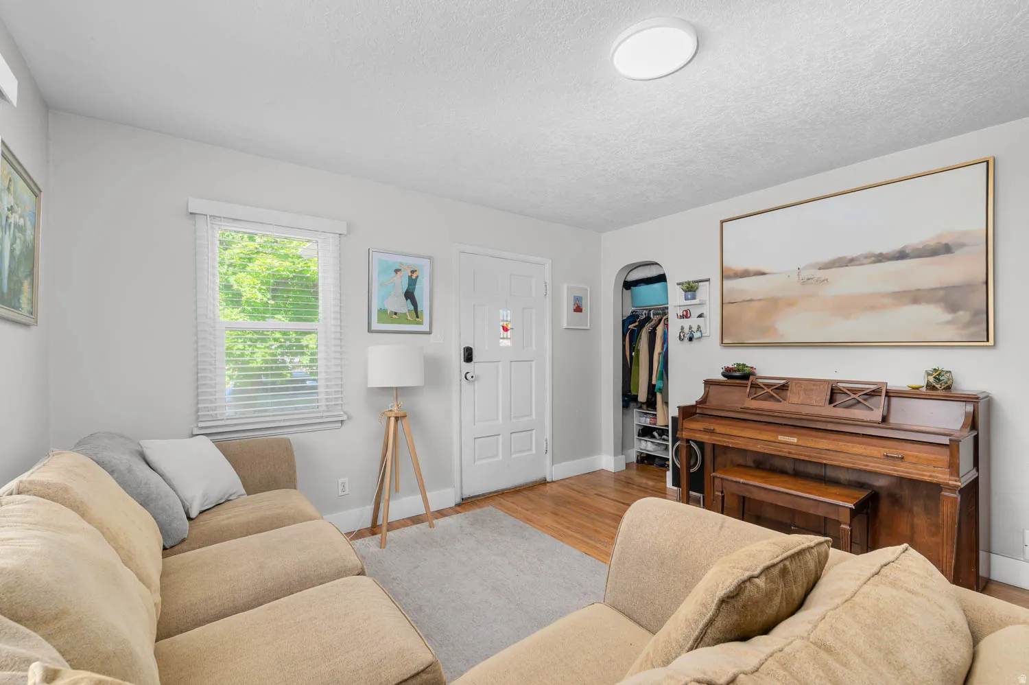 Living area featuring light gray walls, wood-finish flooring, and a large window with blinds