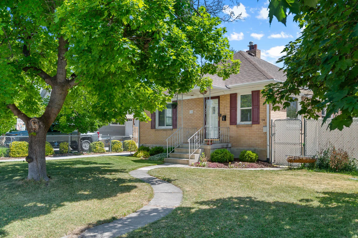 Brick facade residence featuring a front lawn with mature trees and a winding paved walkway