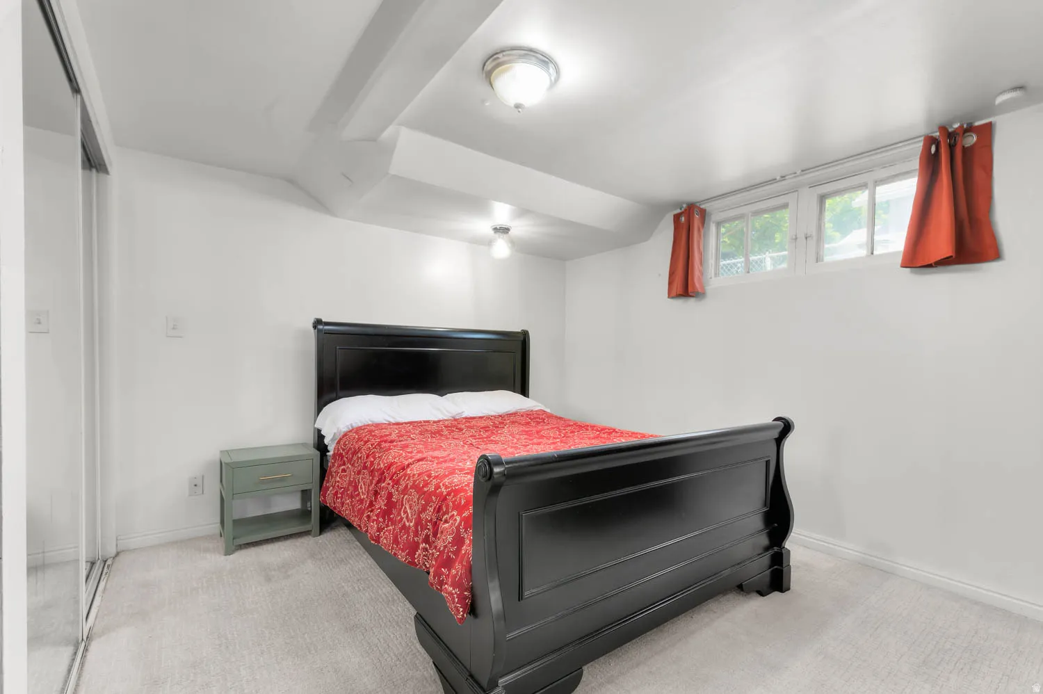 Carpeted interior space featuring white walls and a white ceiling with exposed beams