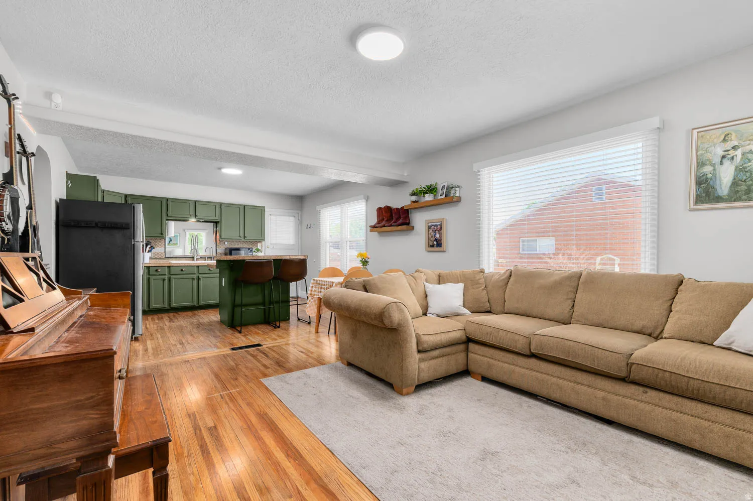 Open-concept living space featuring wood-finish flooring, a kitchen with green cabinetry, a breakfast bar, and a large window