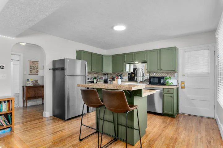 Kitchen featuring sage green cabinetry, stainless steel appliances, a breakfast bar with stone-finish countertop, and wood-finish flooring