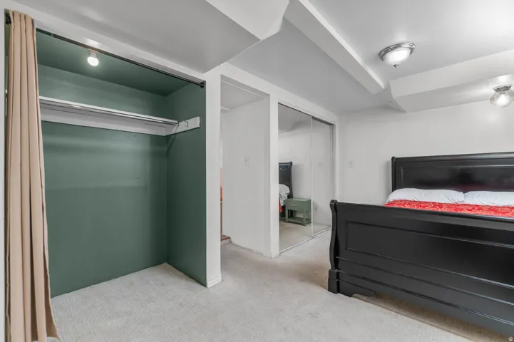 Carpeted room featuring a built-in closet with green interior walls, overhead lighting, and a clothing rod