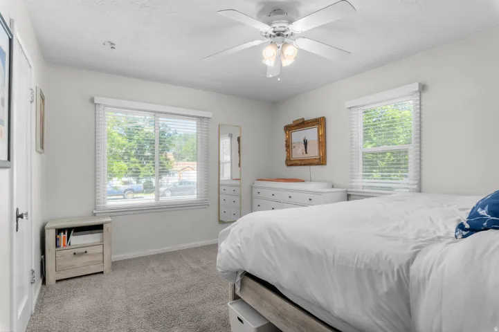 Wall-to-wall carpeting and white walls enhance this space, featuring two windows with horizontal blinds