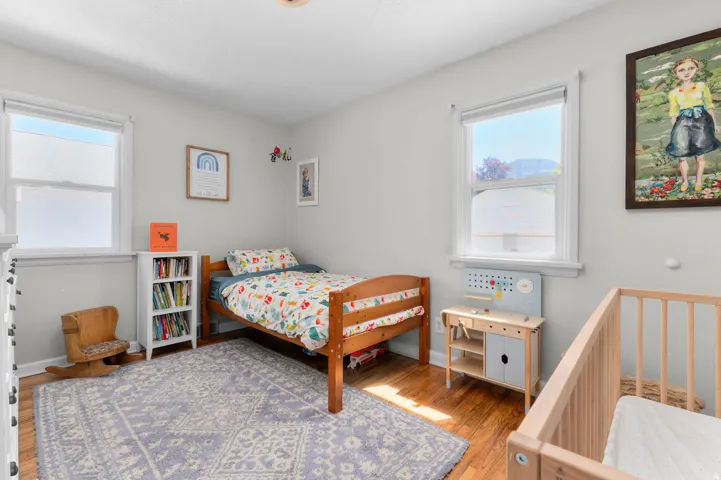 Bright room featuring two windows, light gray walls, and wood-finish flooring