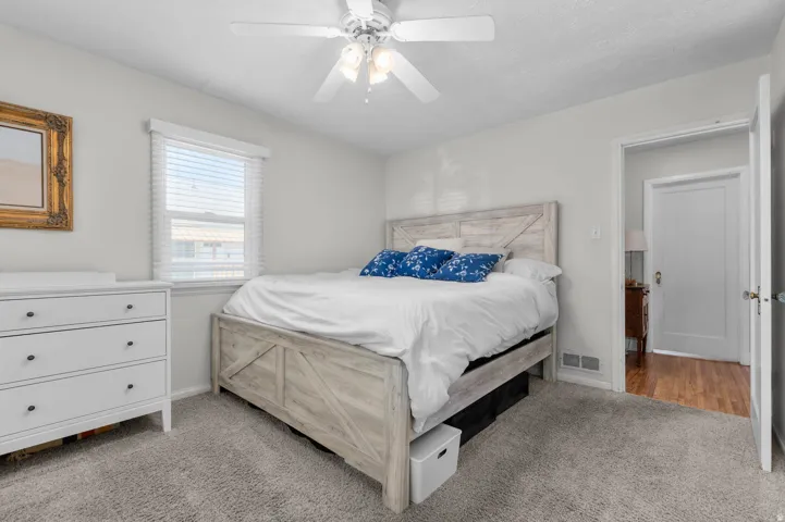 Bedroom featuring light gray wall paint, gray carpet flooring, a window with horizontal blinds, and a ceiling fan with light fixture