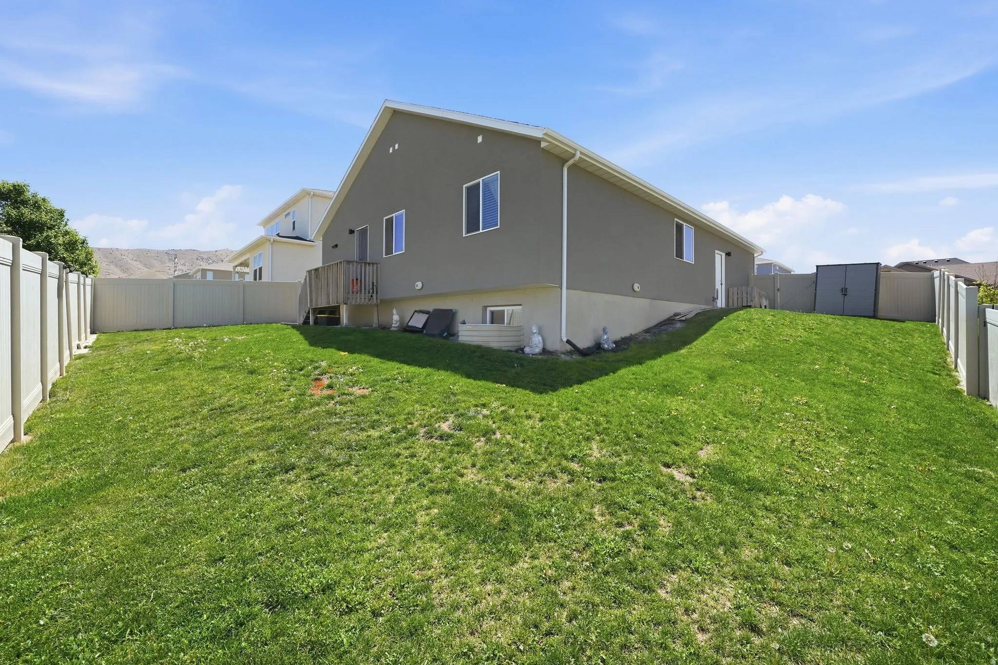 Expansive grassy yard enclosed by a light-colored privacy fence, featuring a grey exterior with white trim