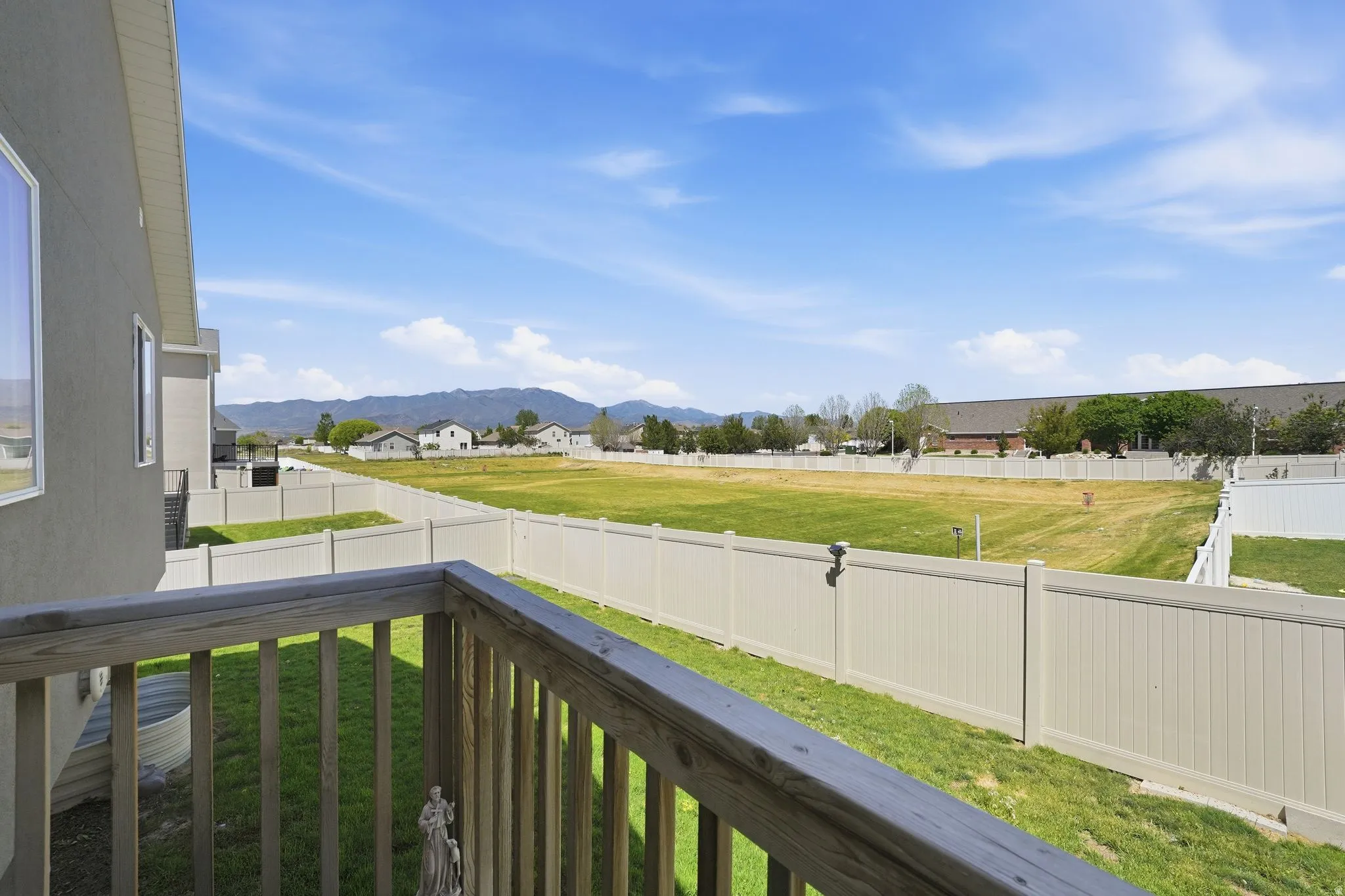 Upper-level balcony with wood railing, offering a broad perspective of the landscaped backyard and surrounding green space