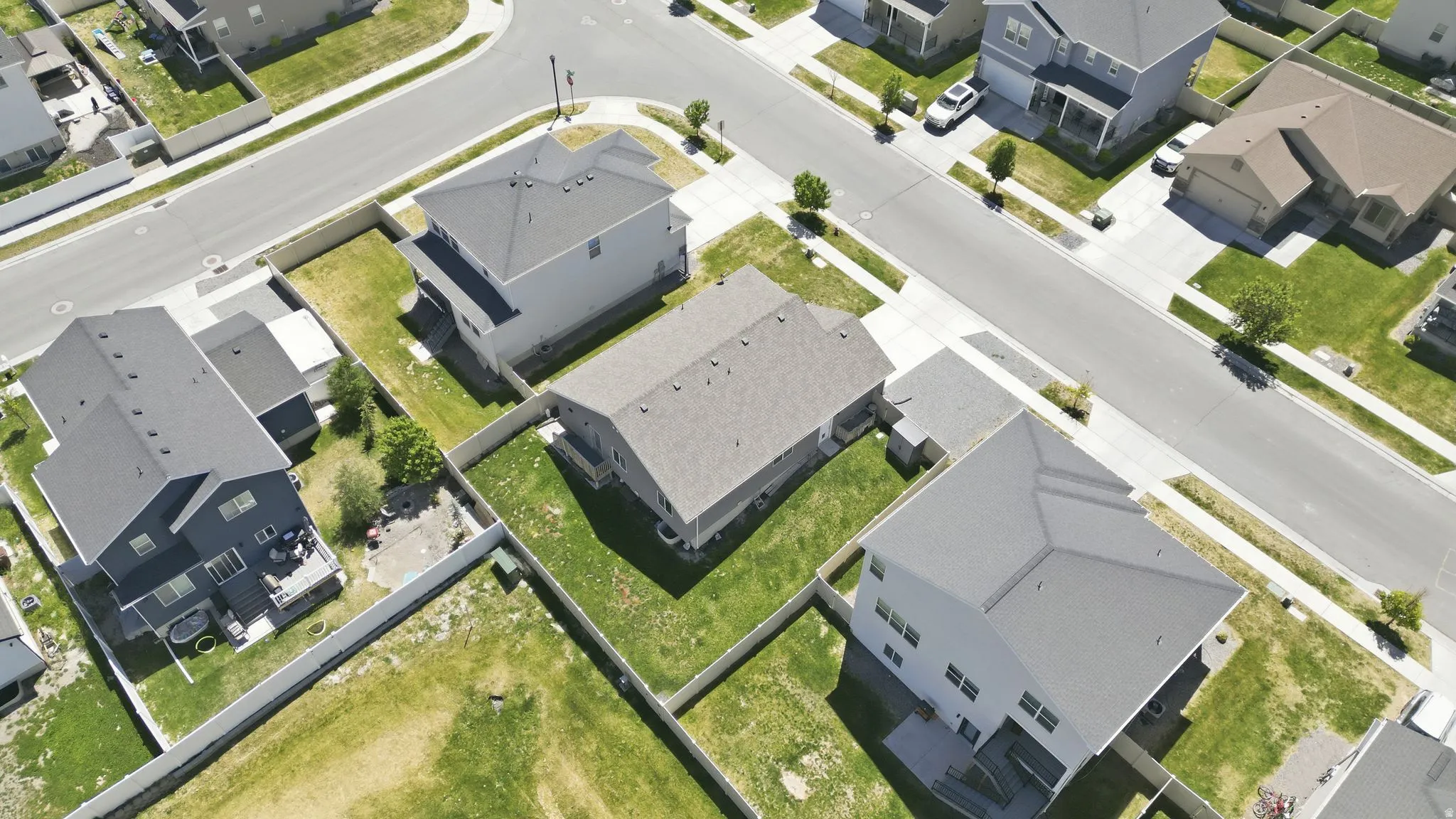 Aerial perspective of a residential neighborhood featuring asphalt streets, concrete sidewalks, and a variety of detached homes with fenced yards
