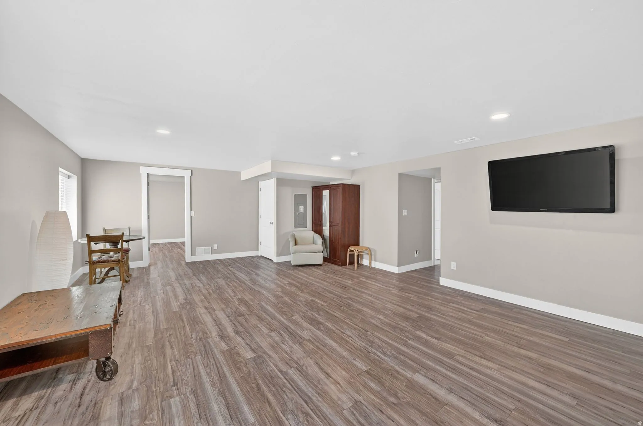 Spacious room featuring wood-finish flooring, recessed lighting, neutral paint, white trim, and a wall-mounted television