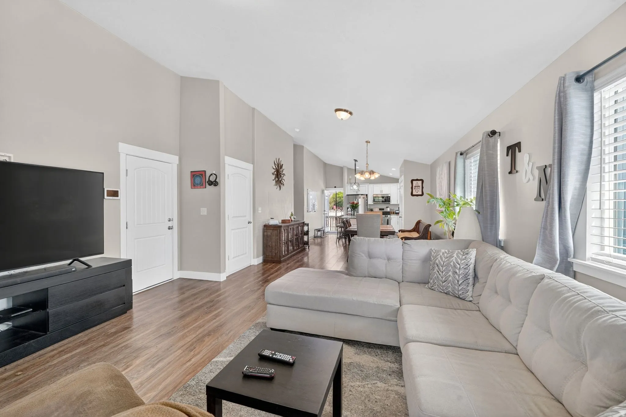 Open concept living area featuring wood-finish flooring, high vaulted ceilings, white trim, and multiple windows with horizontal blinds