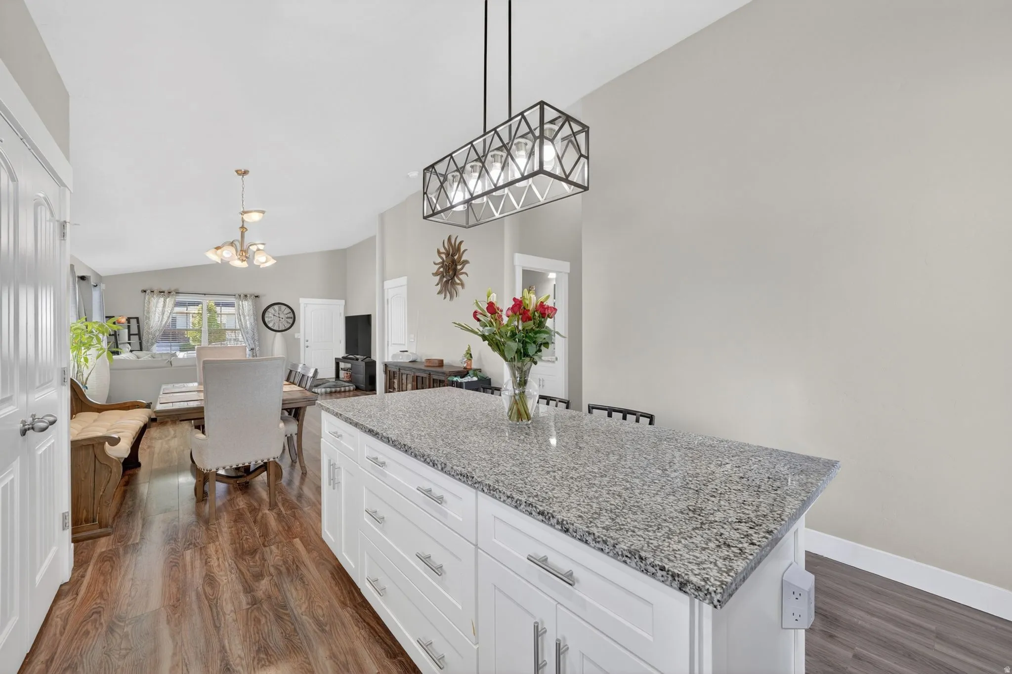 Kitchen island featuring a granite-style countertop, white cabinetry with silver-tone hardware, and a modern rectangular pendant light