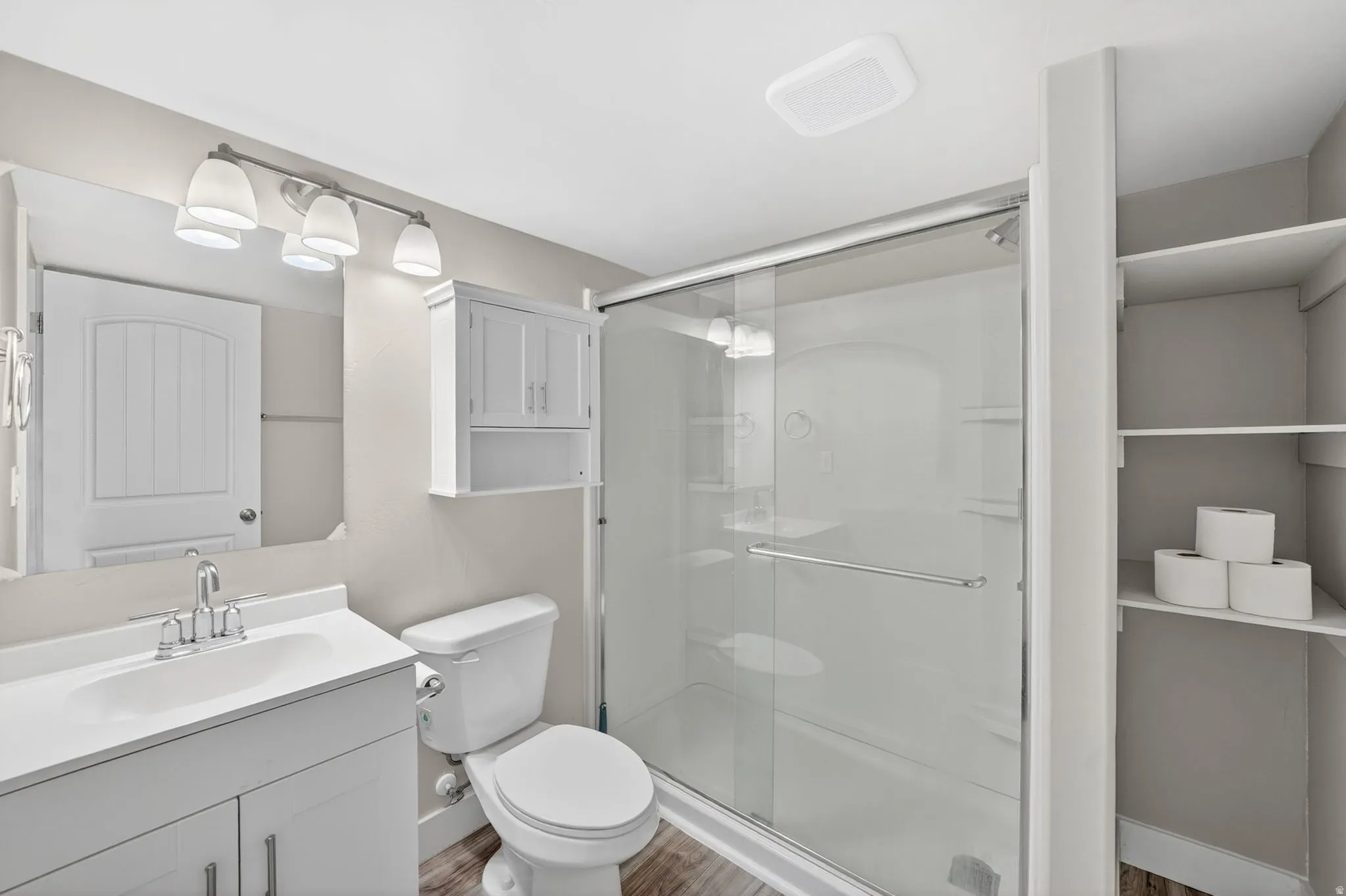 White vanity with integrated sink, coordinating wall-mounted storage cabinet, shower with sliding glass enclosure, and built-in shelving