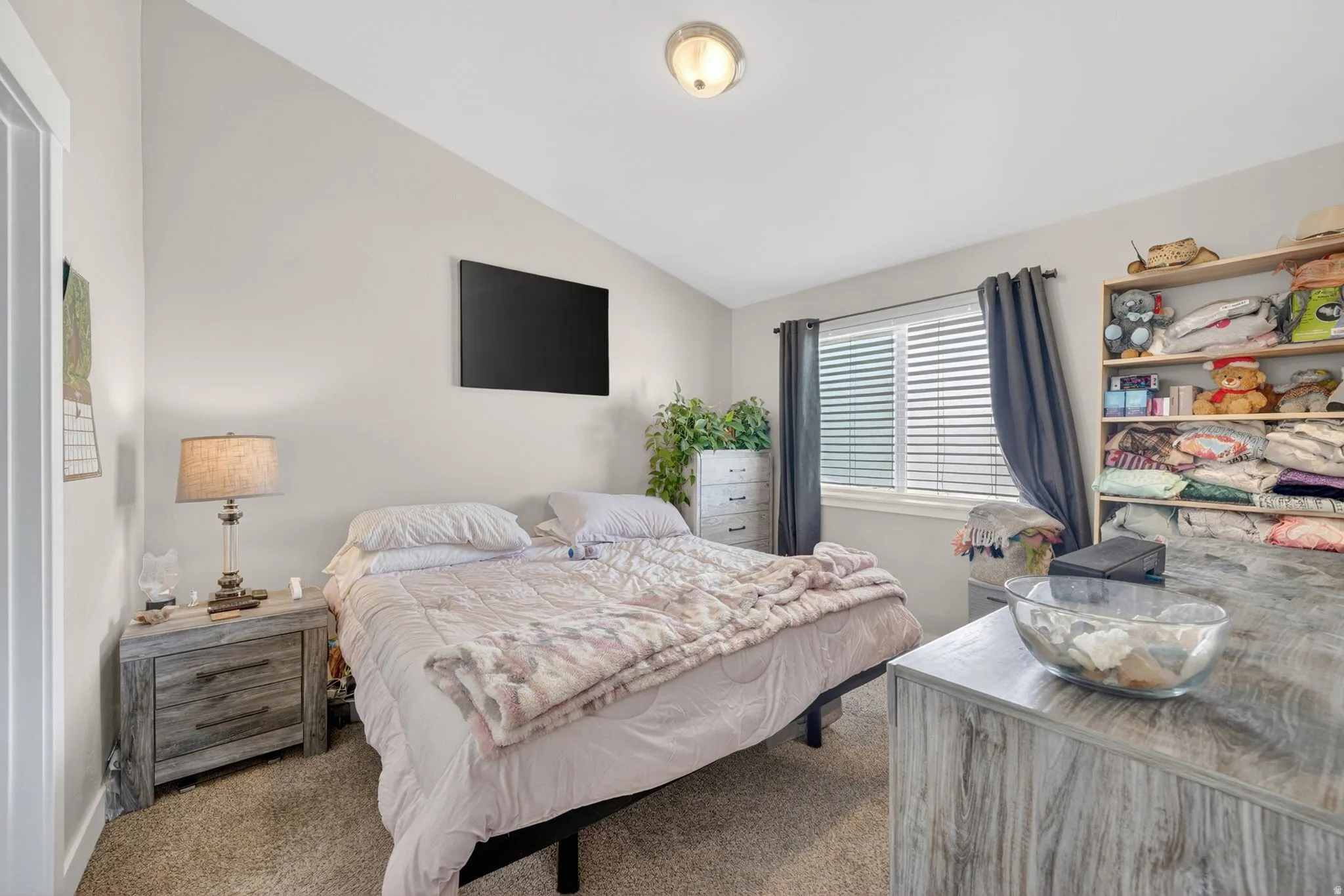 Carpeted bedroom featuring a vaulted ceiling and a single window with blinds