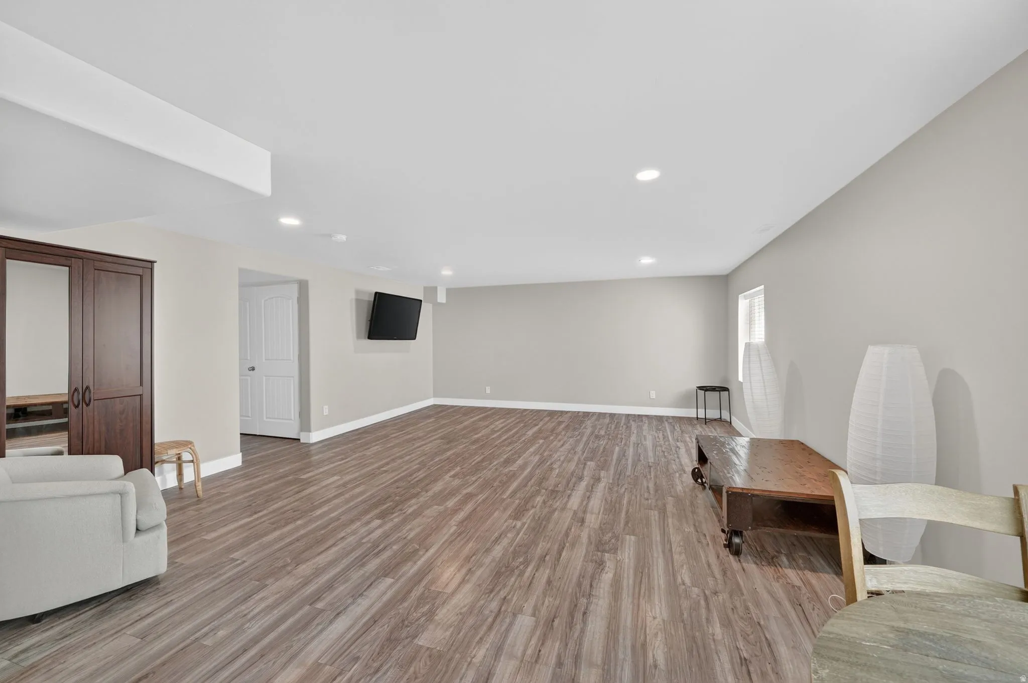 Spacious entertainment area featuring wood-finish flooring, recessed lighting, and light gray wall tones