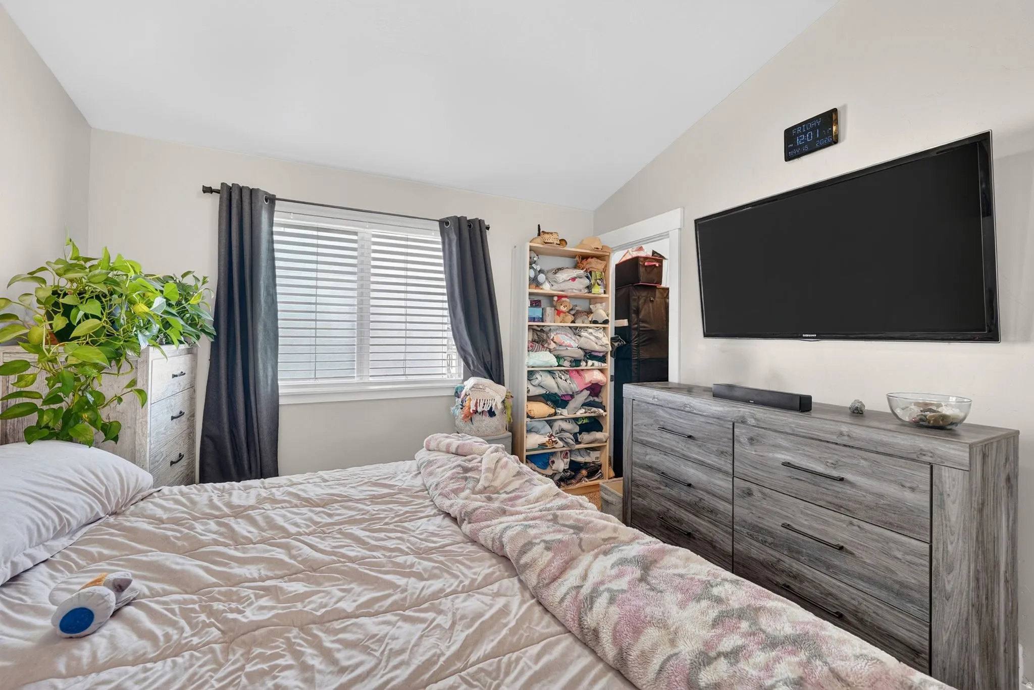 Bedroom featuring an angled ceiling, window with blinds and dark drapes, and a wall-mounted television