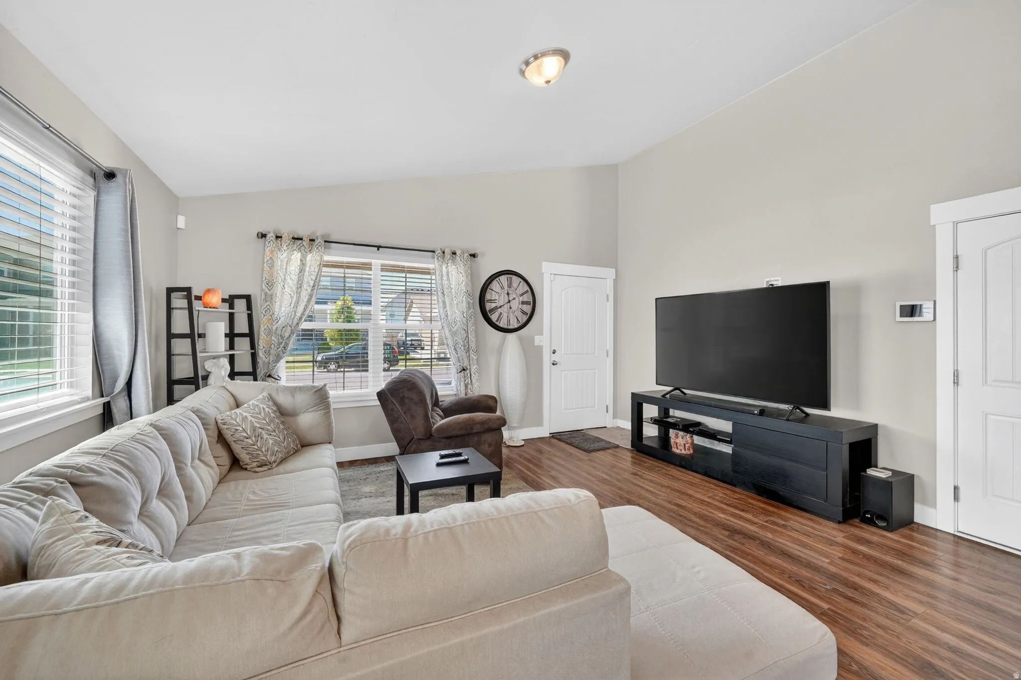 Spacious living area featuring wood-finish flooring, light-toned walls, and multiple windows