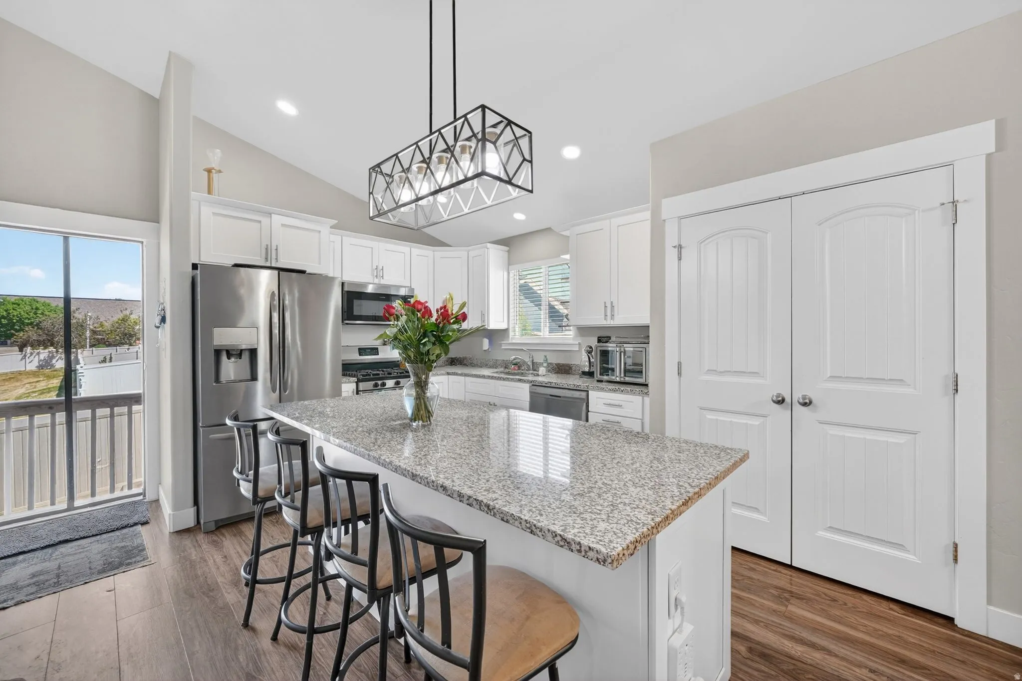 Kitchen featuring a granite-topped island with seating, stainless steel appliances, white cabinetry, and wood-finish flooring