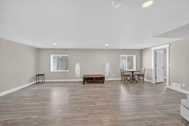 Spacious room featuring wood-finish flooring, recessed lighting, and two windows with horizontal blinds