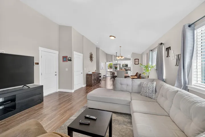 Open concept living area featuring wood-finish flooring, high vaulted ceilings, white trim, and multiple windows with horizontal blinds