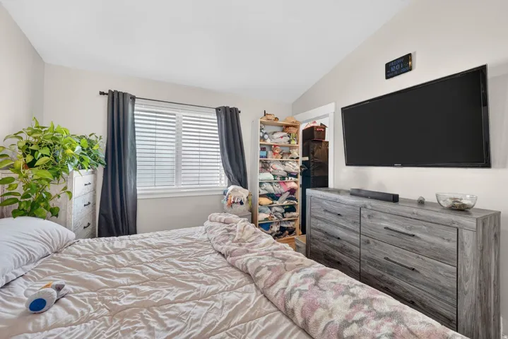 Bedroom featuring an angled ceiling, window with blinds and dark drapes, and a wall-mounted television