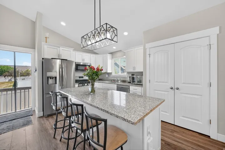 Kitchen featuring a granite-topped island with seating, stainless steel appliances, white cabinetry, and wood-finish flooring
