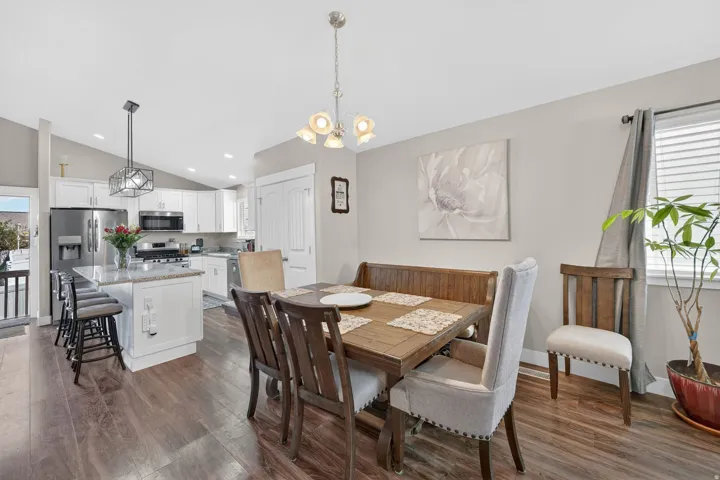 Open-concept living space featuring wood-finish flooring, a kitchen island with seating, white cabinetry, stainless steel appliances, and a dining area with a chandelier