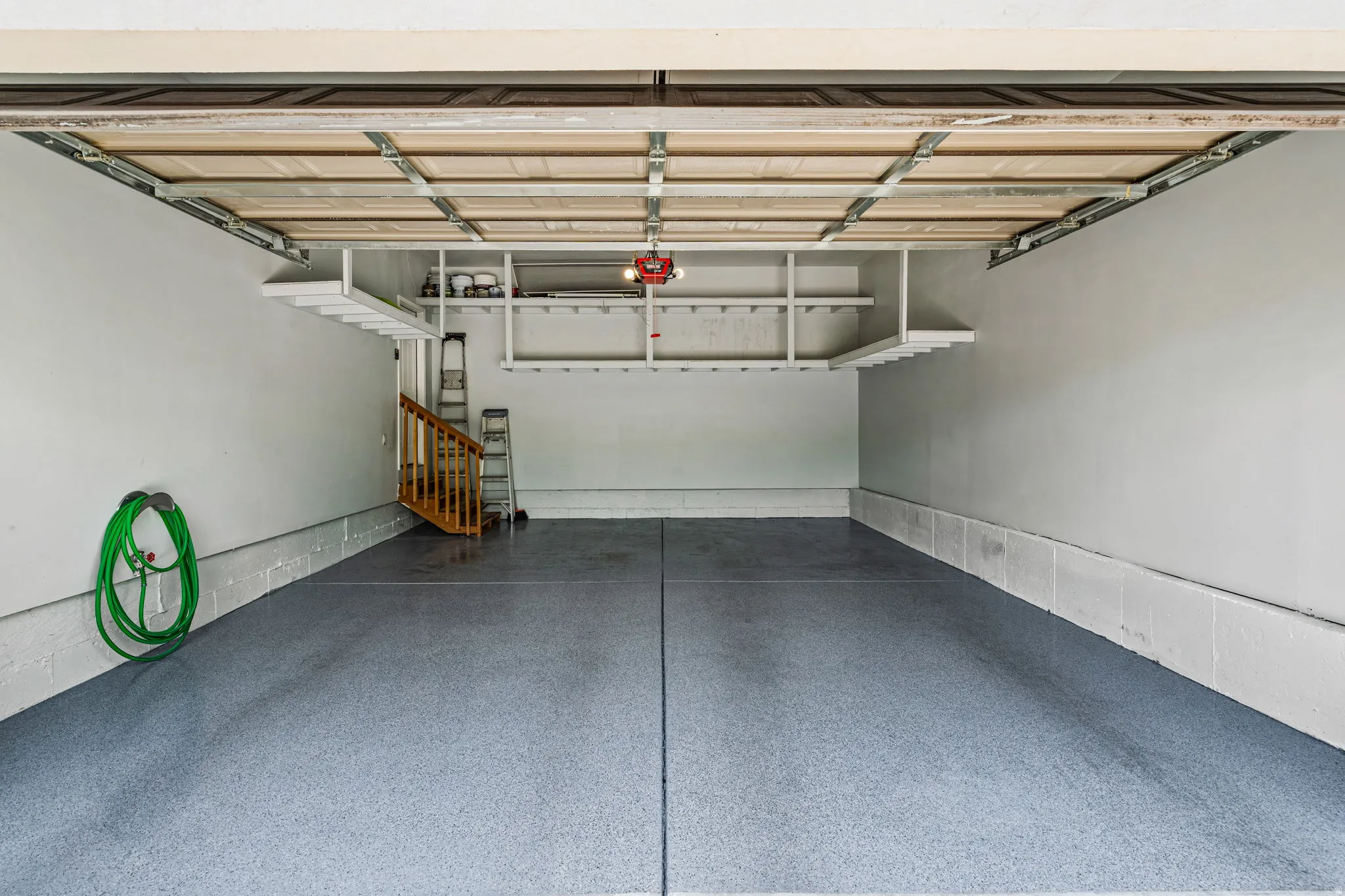 Spacious garage with light grey epoxy flooring, white painted walls, and built-in overhead shelving for organized storage
