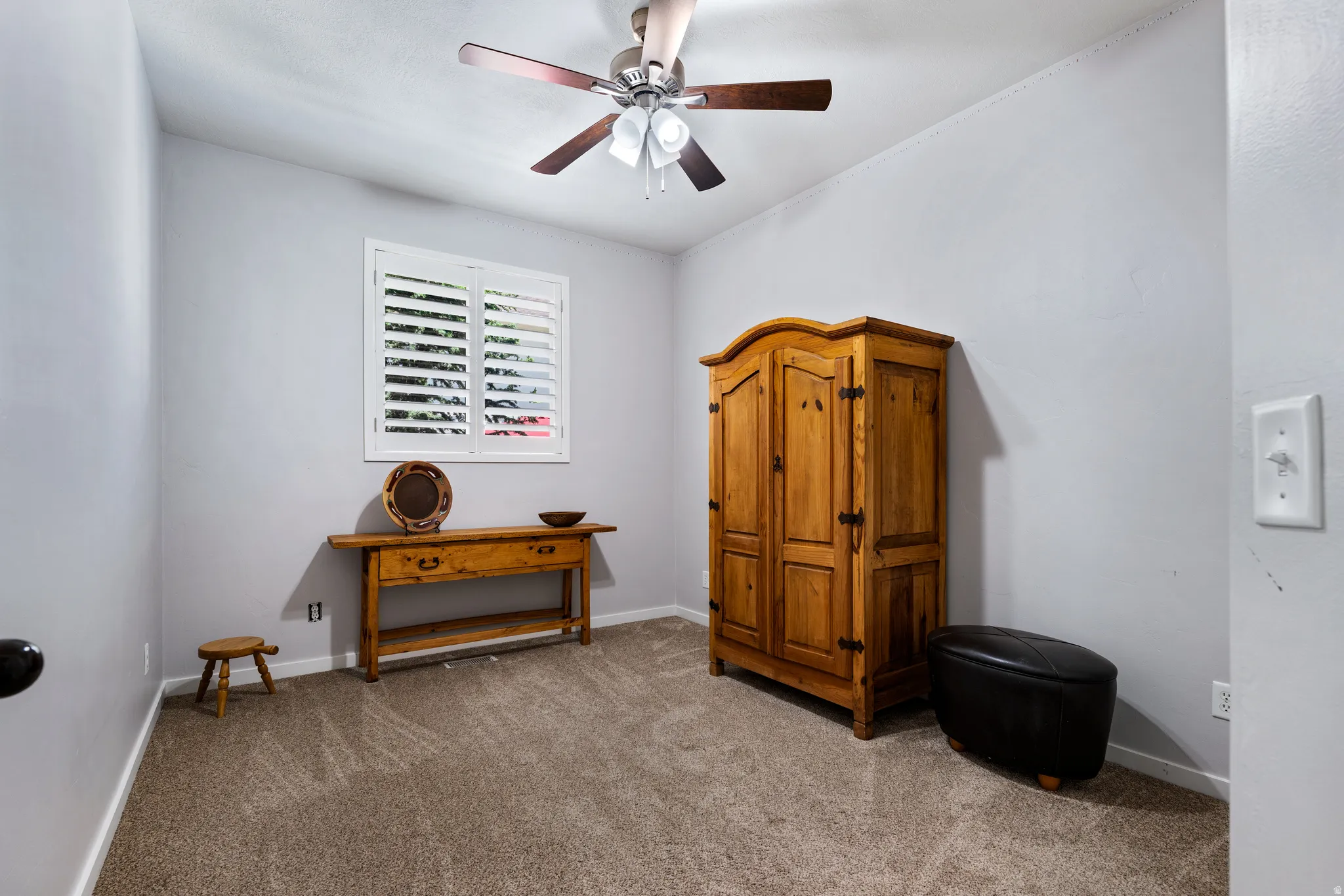 Room featuring neutral gray walls, textured carpet flooring, and a ceiling fan with integrated lighting