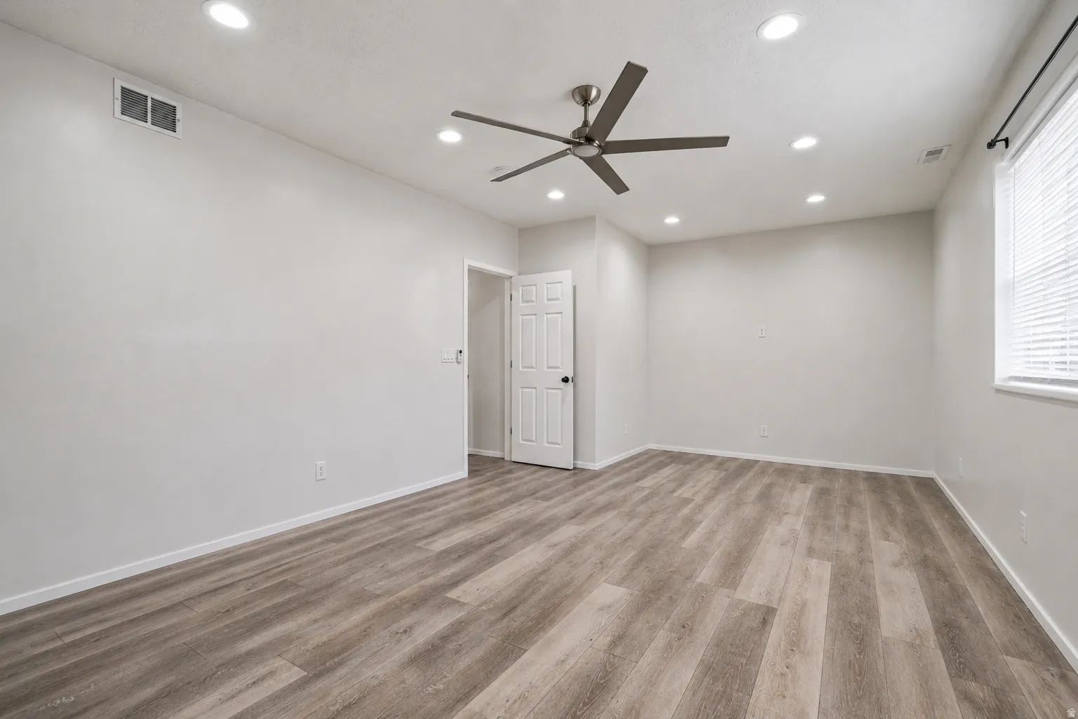 Spacious interior room featuring wood-finish flooring, recessed lighting, and a modern ceiling fan