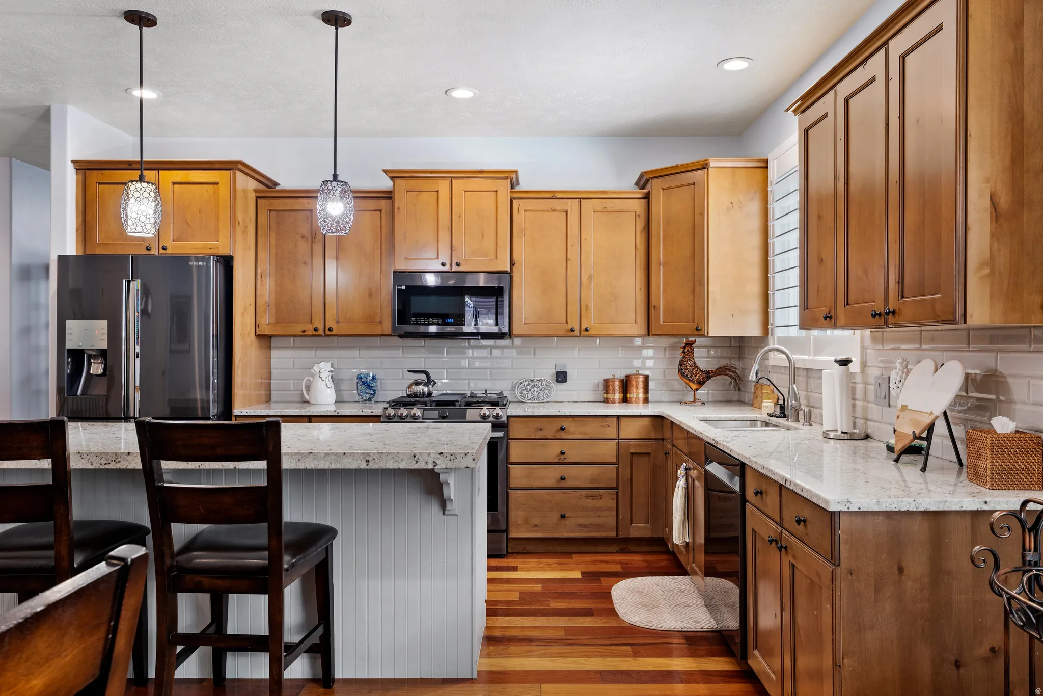 Kitchen featuring wood-finish flooring, light wood cabinetry, white subway tile backsplash, and light-toned countertops