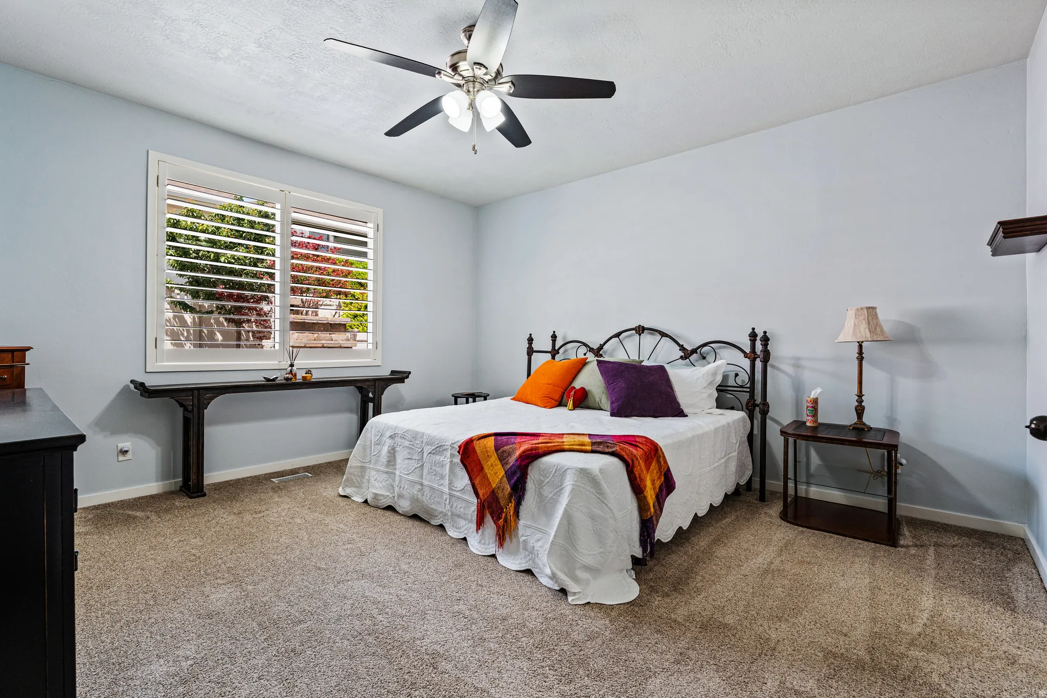 Bedroom featuring a ceiling fan with light kit, plantation shutters, and light-toned carpeting
