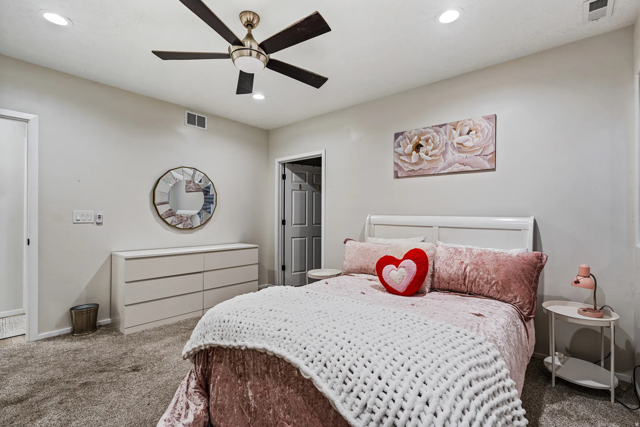 Recessed lighting illuminating a spacious room with light gray walls, a ceiling fan with dark wood-finish blades, and soft gray carpeting