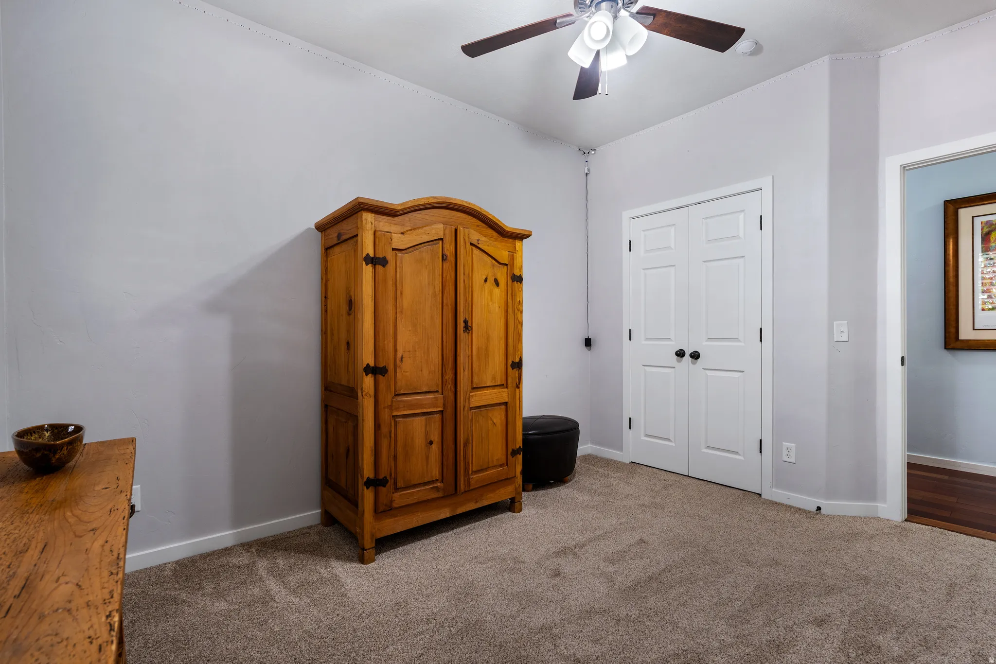 Carpeted room featuring a ceiling fan with light fixture, white interior doors, and light gray wall paint