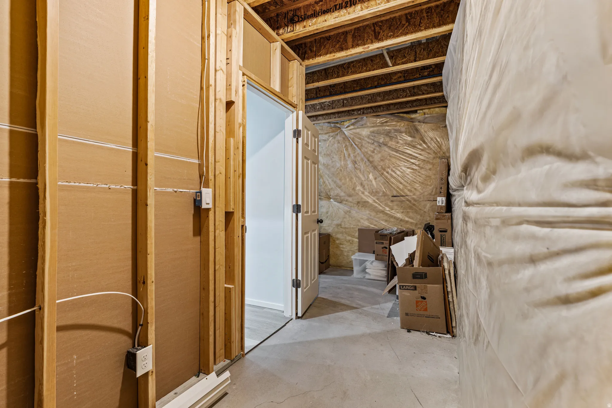 Unfinished basement area featuring exposed wood framing, concrete flooring, exposed ceiling joists, and a partial vapor barrier installation