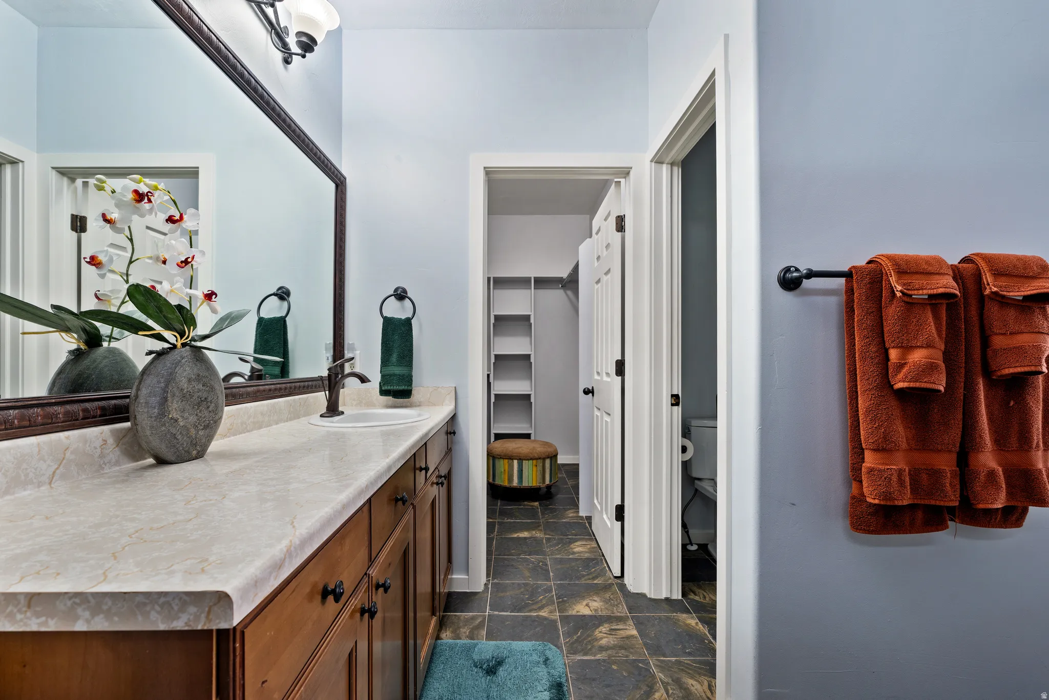 Bathroom featuring a dual-sink vanity with a beige countertop, dark wood-finish cabinetry, and an expansive wall mirror