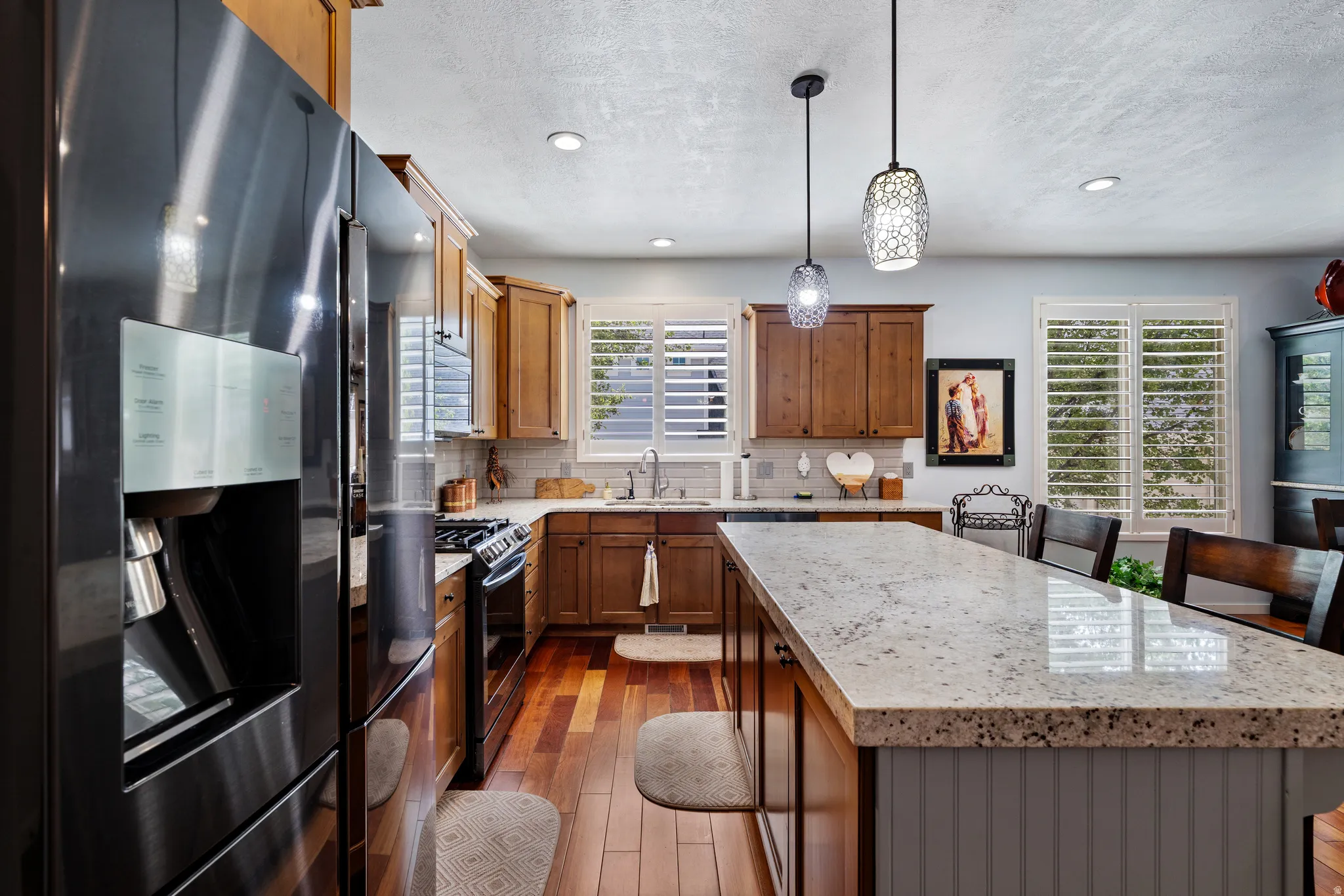 Kitchen featuring stainless steel appliances, wood-finish flooring, wood cabinetry, light-toned countertops, and plantation shutters