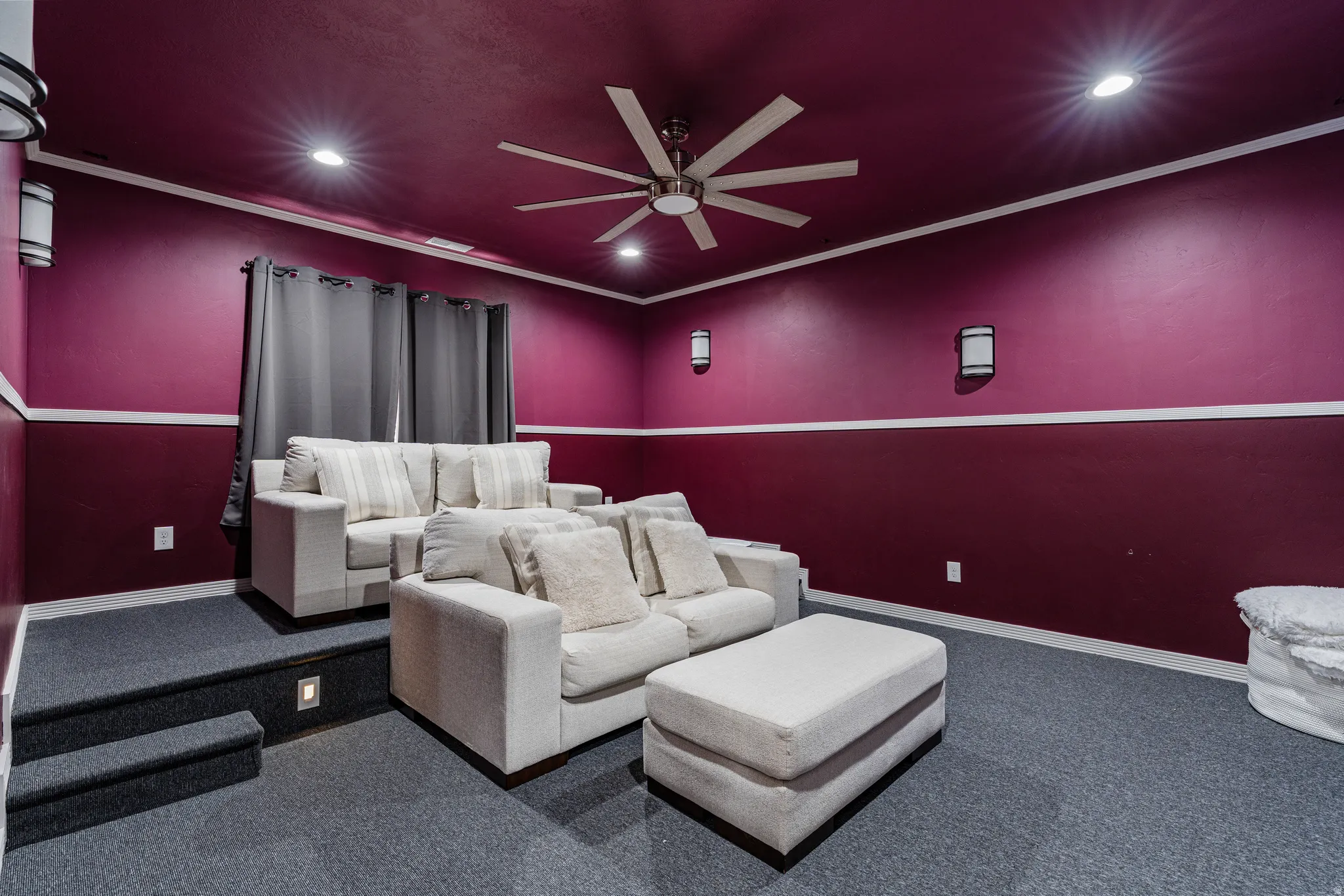 Media room featuring tiered seating, recessed ceiling lights, wall sconces, a ceiling fan, and dark purple walls with white trim