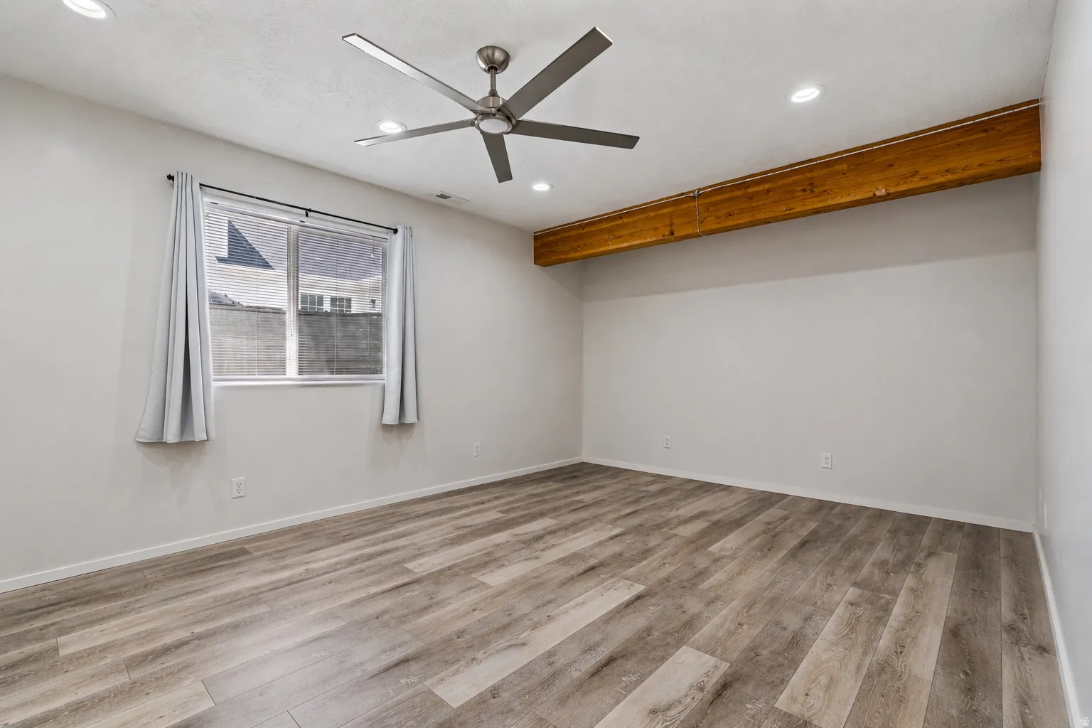 Spacious room featuring wood-finish flooring, a modern ceiling fan, recessed lighting, and a prominent wood beam accent