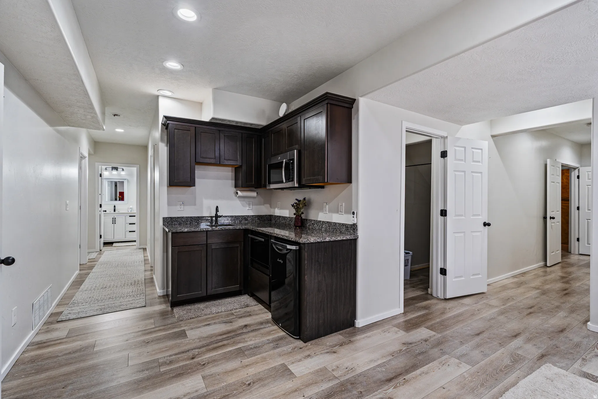 Compact kitchen area featuring dark wood-finish cabinetry, a black appliance package including a microwave and dishwasher, and speckled countertops
