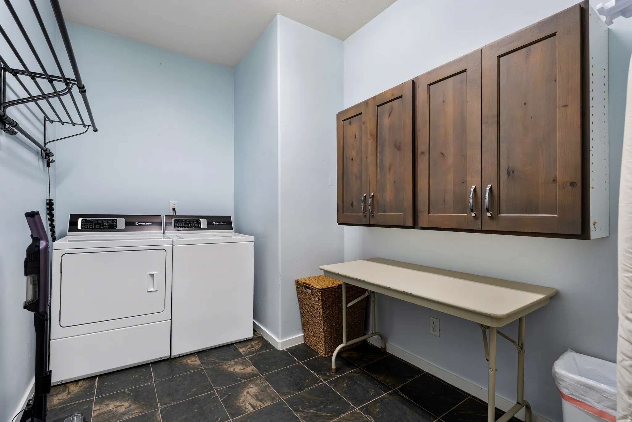 Laundry room featuring slate-style flooring, light blue walls, and dark wood-finish cabinetry