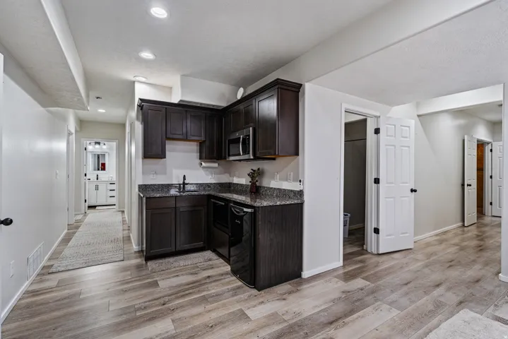 Compact kitchen area featuring dark wood-finish cabinetry, a black appliance package including a microwave and dishwasher, and speckled countertops