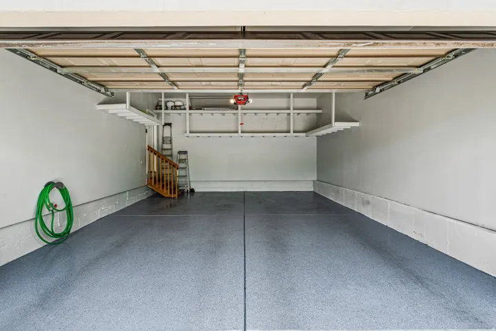 Spacious garage with light grey epoxy flooring, white painted walls, and built-in overhead shelving for organized storage
