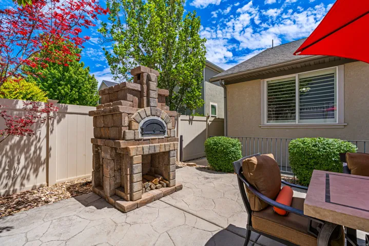 Stone-clad outdoor pizza oven with an arched black door, set on a stamped concrete patio