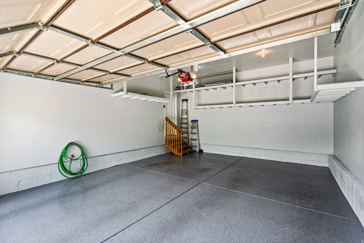 Spacious garage featuring a durable epoxy-coated floor, overhead door, built-in shelving, and a wooden staircase